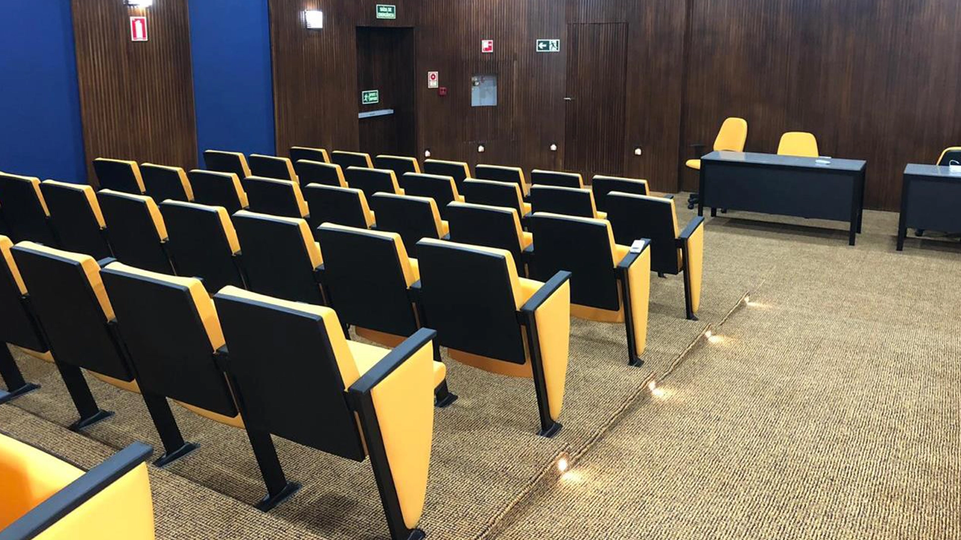 Auditório com mesa de autoridades e cadeiras reservadas ao fundo da sala