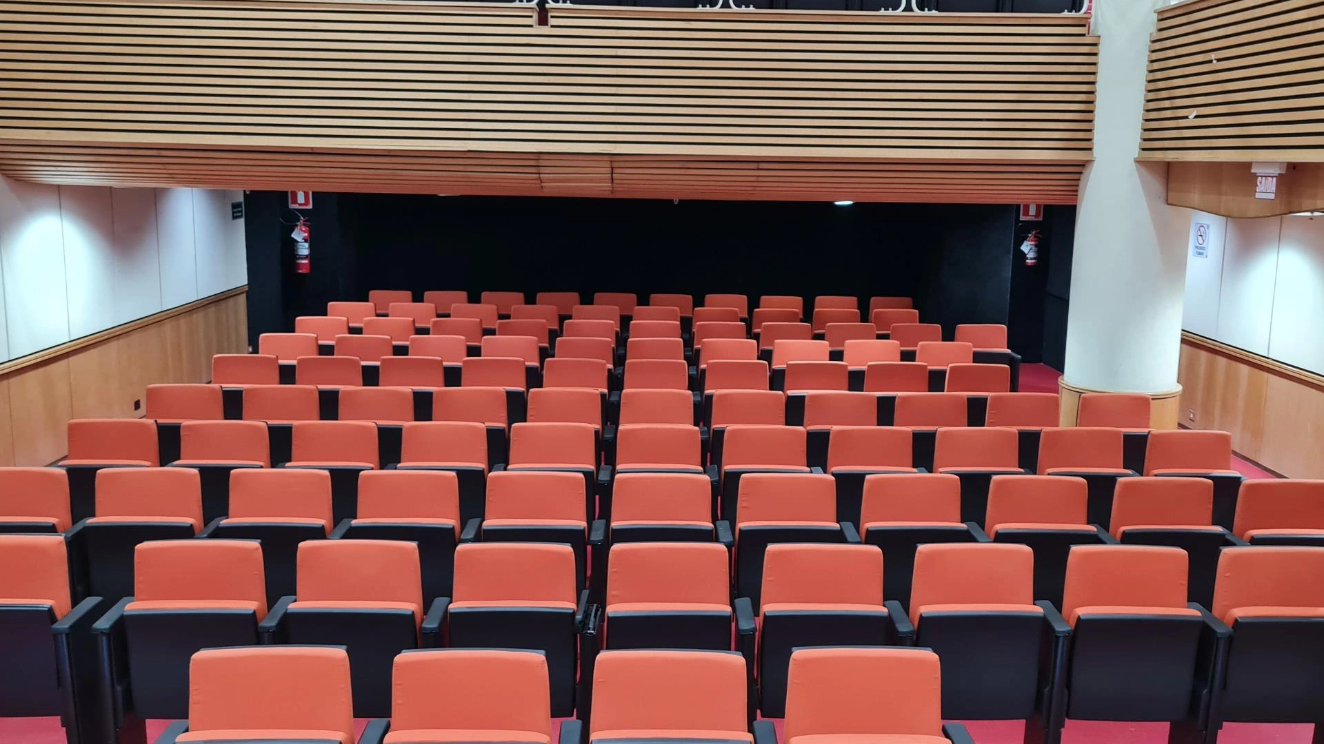 Plateia de auditório com cadeiras estofadas em terracota, vista frontal do palco