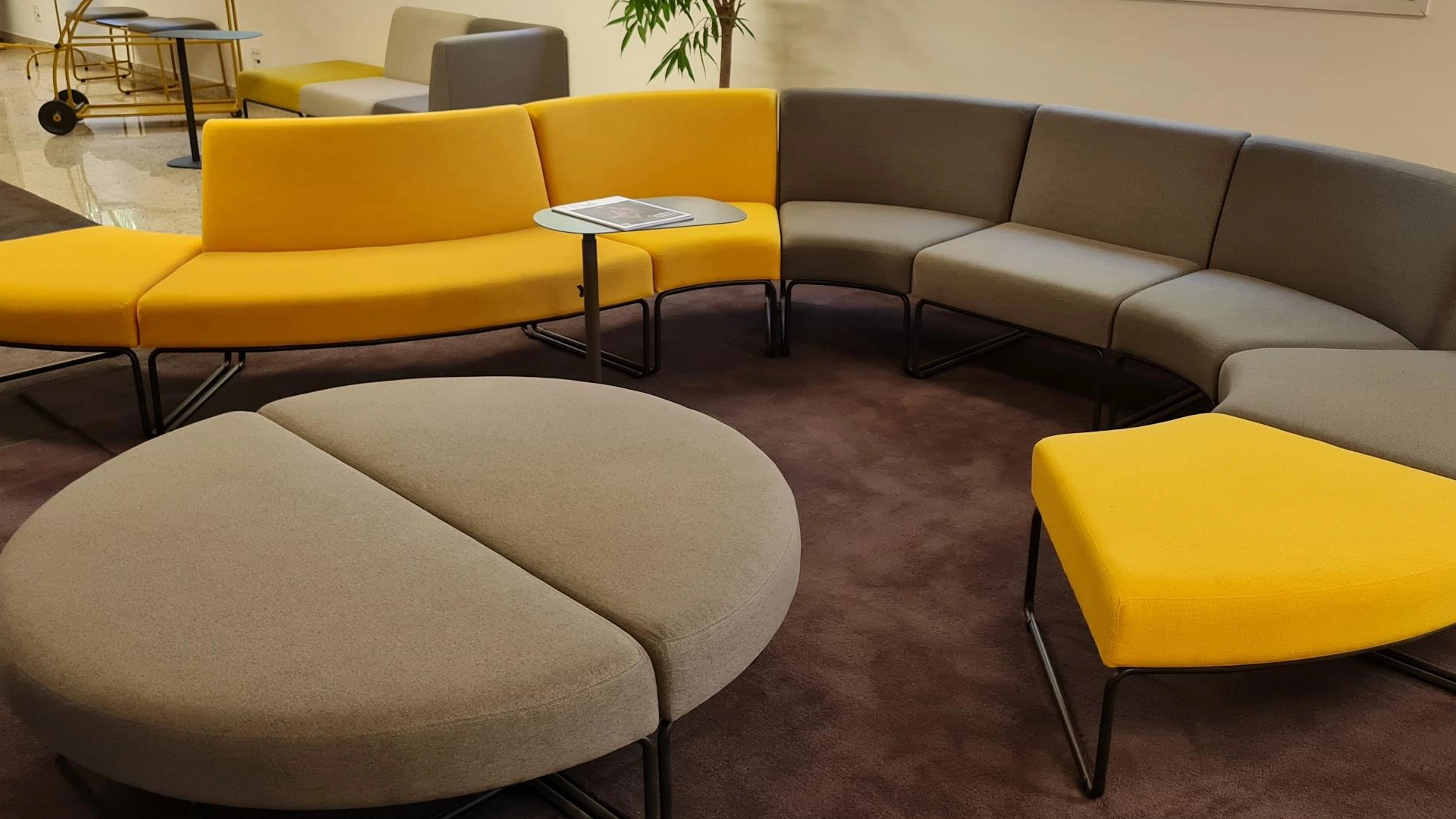 Sofá modular curvo com poufs redondos em amarelo e cinza, área de espera