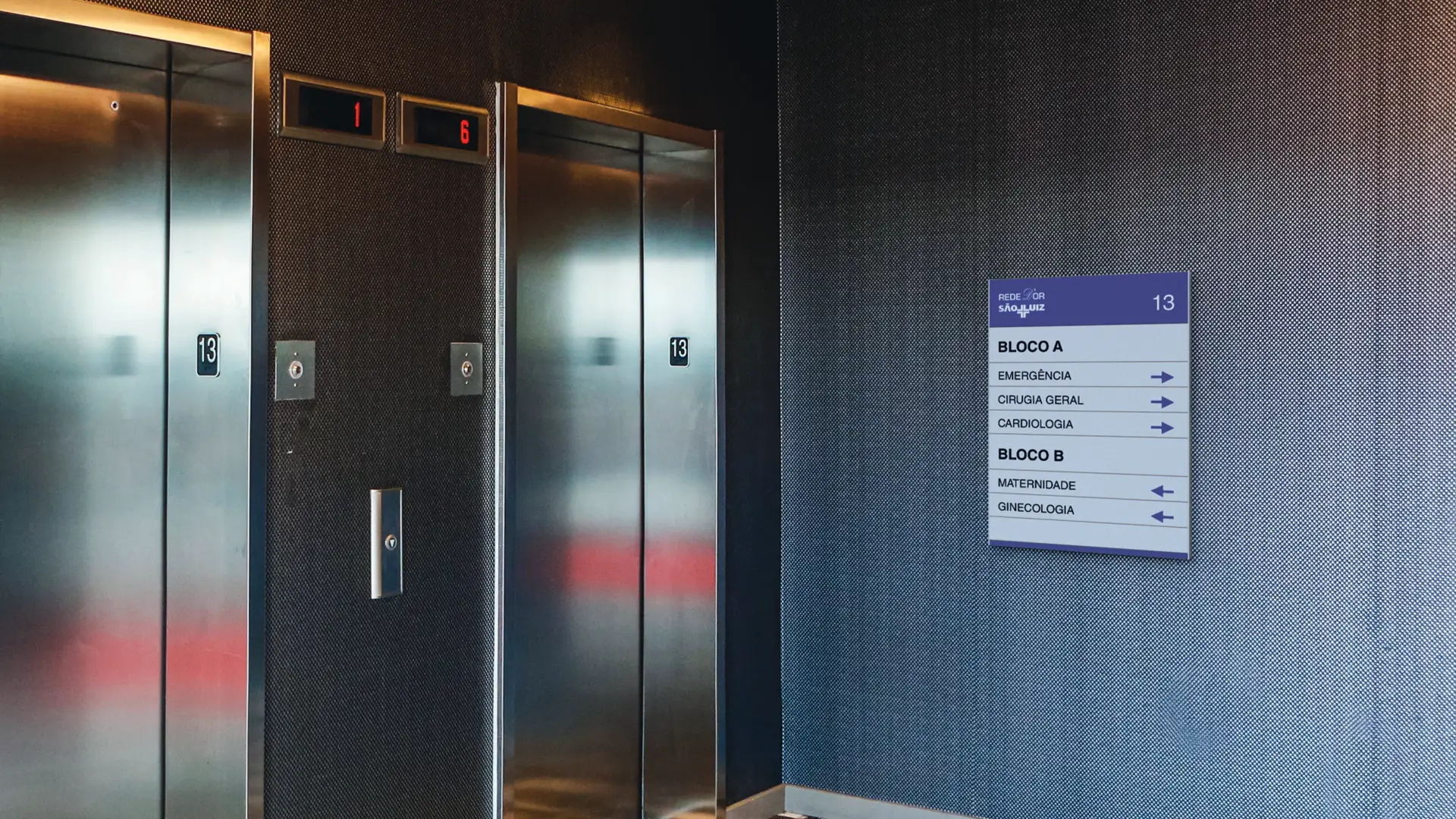 Painel de pavimento ao lado de elevadores, indicando blocos e setores do andar