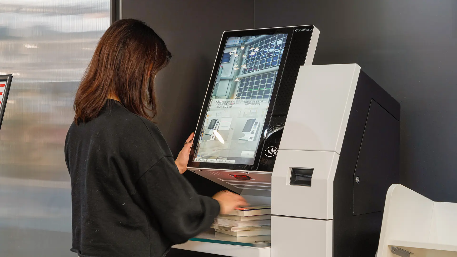 Usuária realizando check-out de livros em quiosque de autoatendimento com leitura RFID